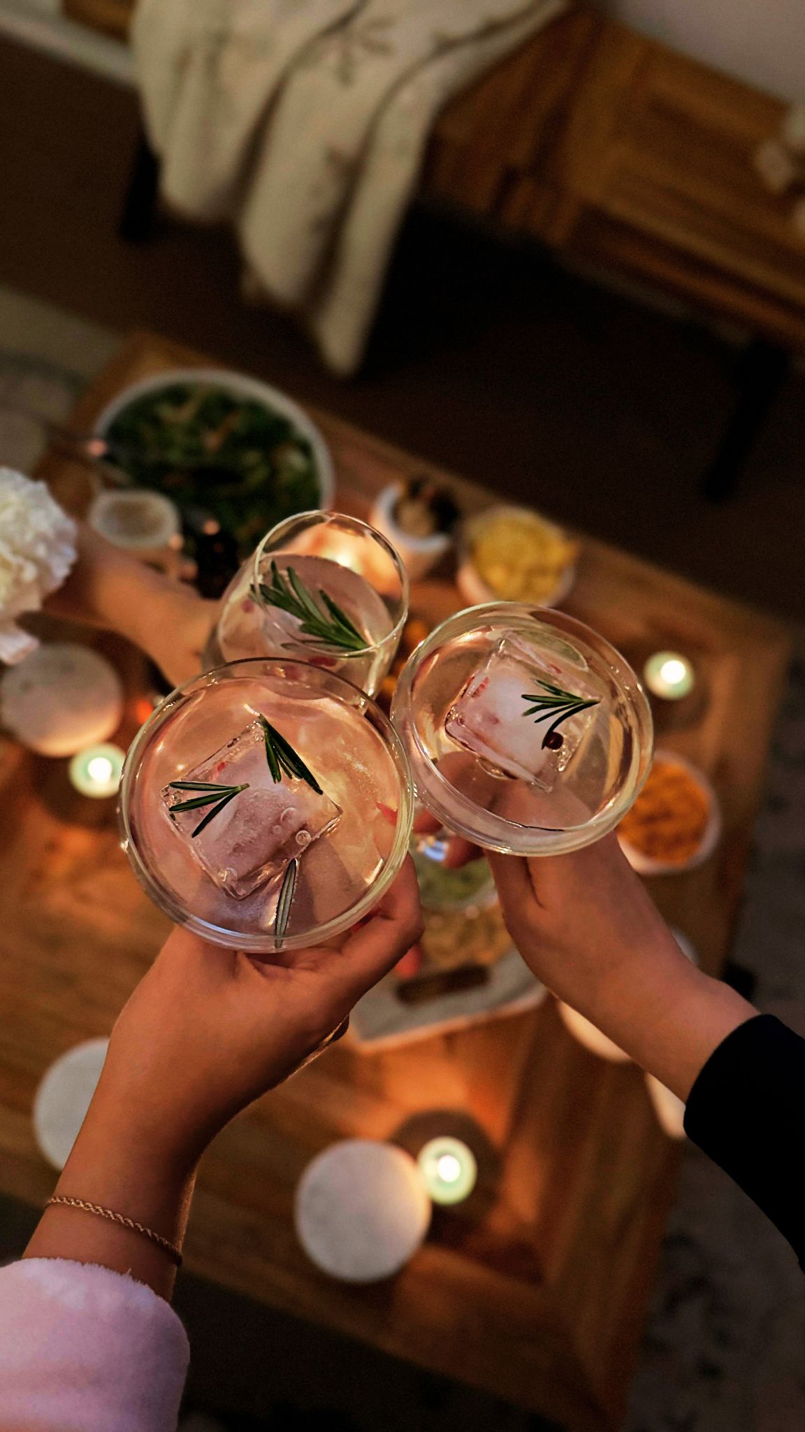 Three people toasting their cocktail drinks over a table filled with food